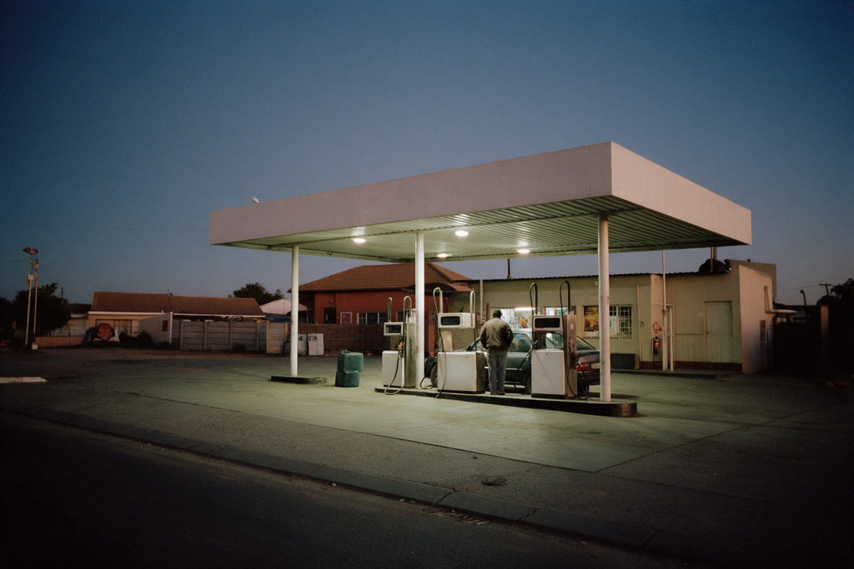 A man filling his car at a small forecourt at dusk
