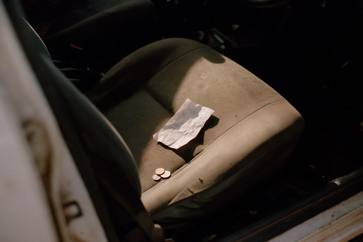 A crumpled till slip and loose coins on a car seat in low sun